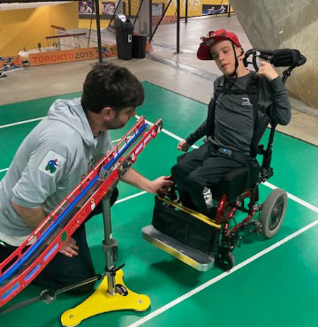A young boccia player practicing, his father helps move his wheelchair